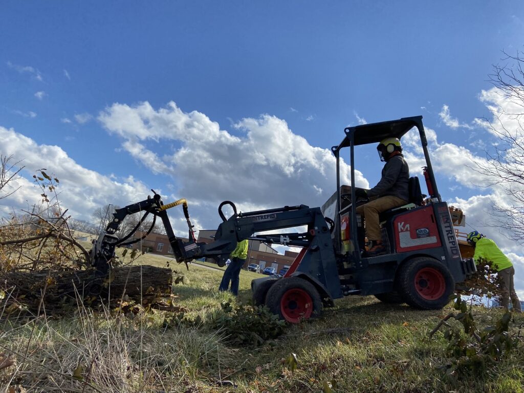 Intrepid KM100 Tele articulating loader with branch manager grapple picking up a log