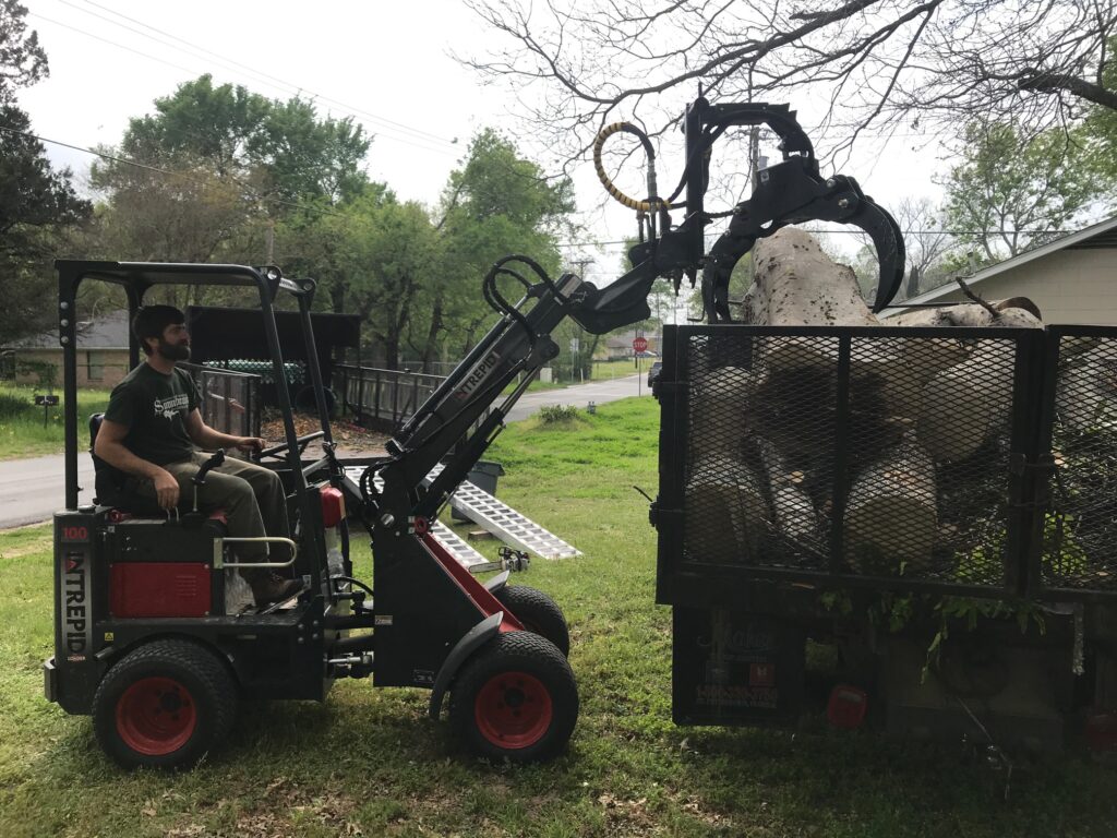 Mini loader loading logs into trailer using Branch Manager grapple