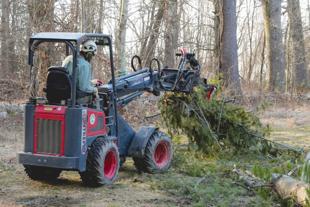 Intrepid KM130 Tele small articulated loader grabbing stack of brush with a log grab.